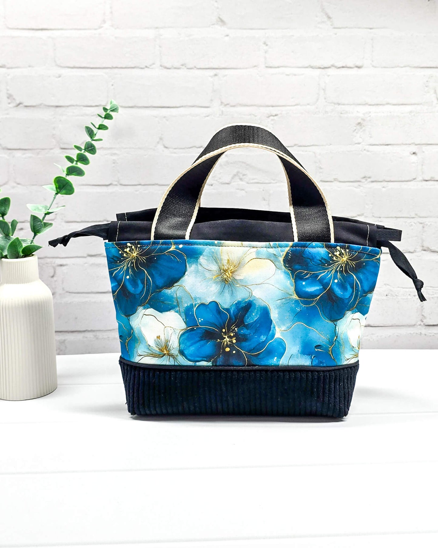 Handgemachte Projekttasche Alva in Größe S mit zwei Tragegriffen, blauen Aquarellblüten und einem Taschenboden aus schwarzem Breitcord. Handgenäht in Bayern von Nadelmikado. 