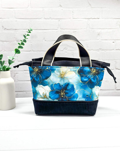 Handgemachte Projekttasche Alva in Größe S mit zwei Tragegriffen, blauen Aquarellblüten und einem Taschenboden aus schwarzem Breitcord. Handgenäht in Bayern von Nadelmikado. 