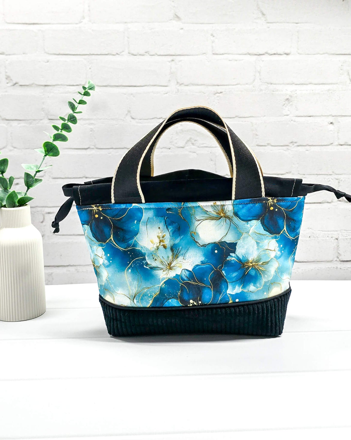 Handgemachte Projekttasche Alva in Größe S mit zwei Tragegriffen, blauen Aquarellblüten und einem Taschenboden aus schwarzem Breitcord. Handgenäht in Bayern von Nadelmikado. 