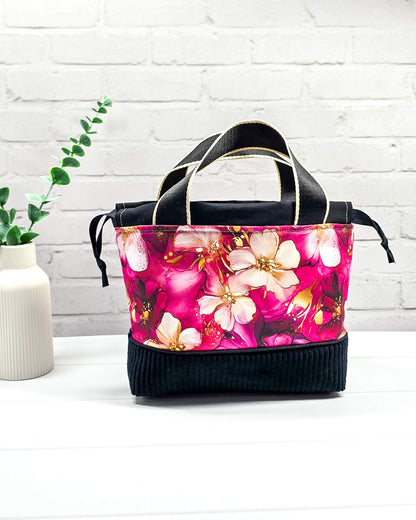 Handgemachte Projekttasche Alva in Größe S mit zwei Tragegriffen, magentafarbenen Aquarellblüten und einem Taschenboden aus schwarzem Breitcord. Handgenäht in Bayern von Nadelmikado. 