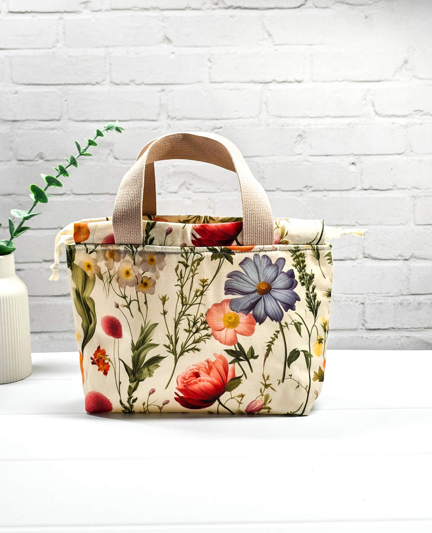 Handgenähte Projekttasche Alva S von Nadelmikado mit feinen botanischen Blumen-Illustrationen auf hellem Stoff, beige Tragehenkel.