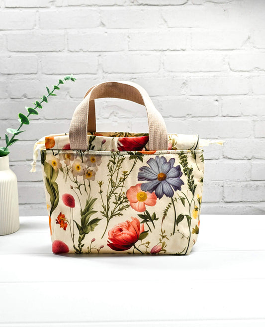 Handgenähte Projekttasche Alva S von Nadelmikado mit feinen botanischen Blumen-Illustrationen auf hellem Stoff, beige Tragehenkel.