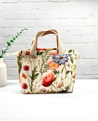Handgenähte Projekttasche Alva S von Nadelmikado mit feinen botanischen Blumen-Illustrationen auf hellem Stoff, beige Tragehenkel.