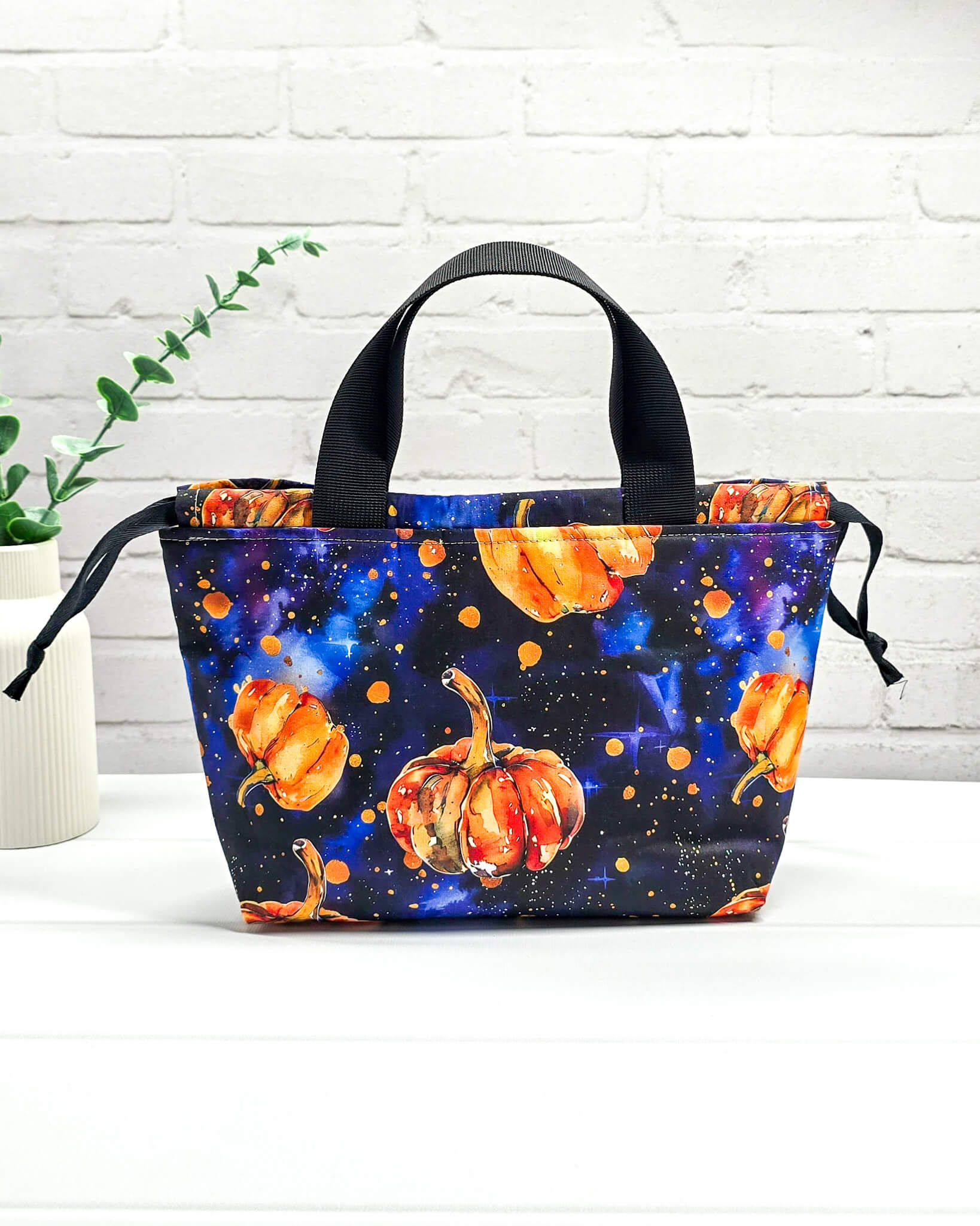 Projekttasche Alva S mit orangefarbenen Kürbissen auf dunkelblauem Galaxie-Sternenhimmel-Stoff und schwarzen Henkeln. Handgenäht in Bayern von Nadelmikado
