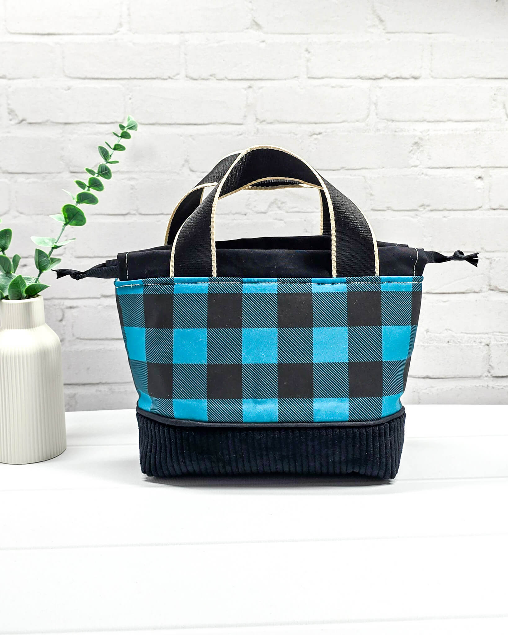 Handgemachte Projekttasche Alva in Größe S mit zwei Tragegriffen, blau-schwarzem Karomuster und einem Taschenboden aus schwarzem Breitcord. Handgenäht in Bayern von Nadelmikado. 