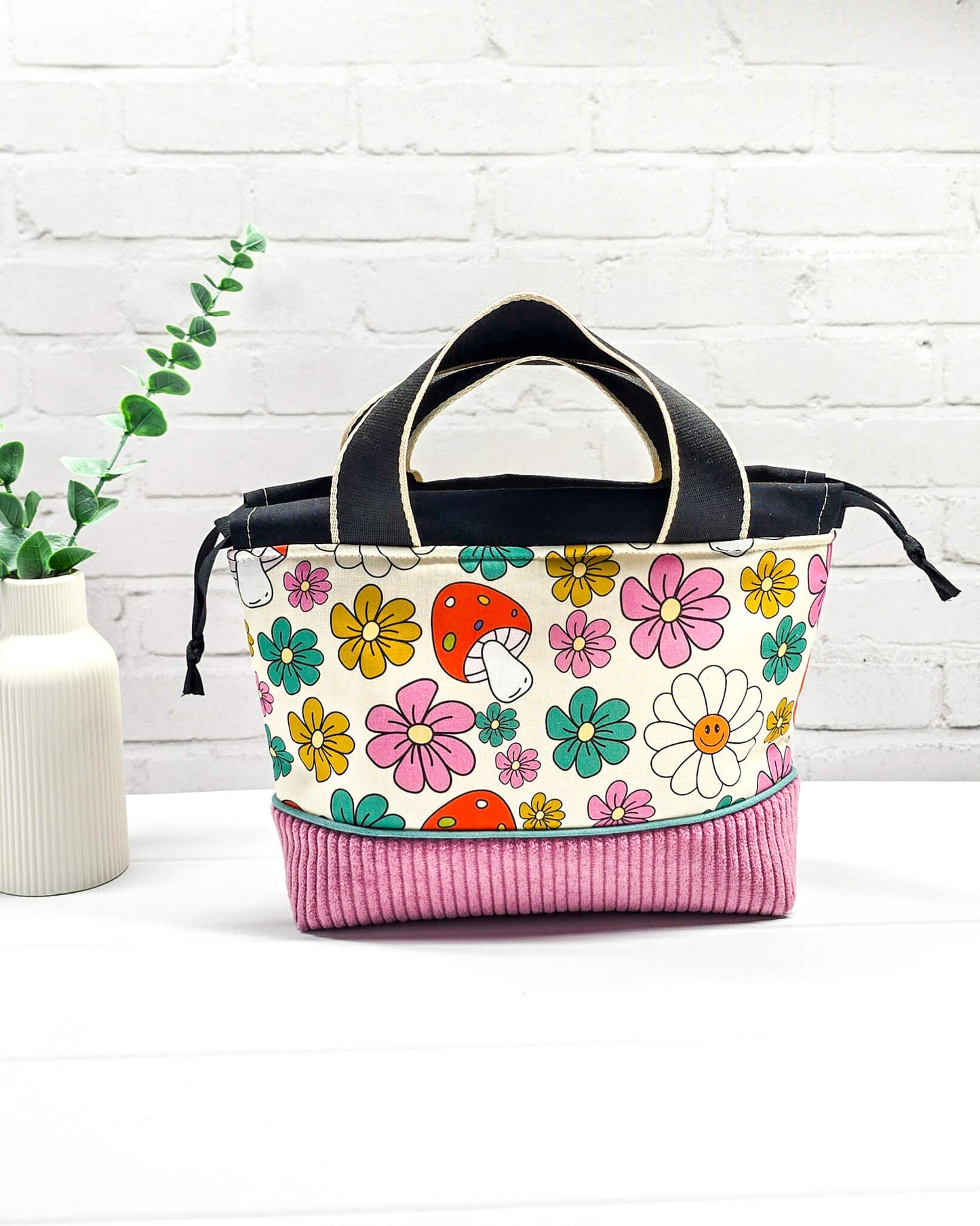 Handgemachte Projekttasche Alva in Größe S mit zwei Tragegriffen, bunten Retro-Pilzen und Blumen auf hellem Stoff und einem Taschenboden aus altrosa Breitcord. Handgenäht in Bayern von Nadelmikado. 