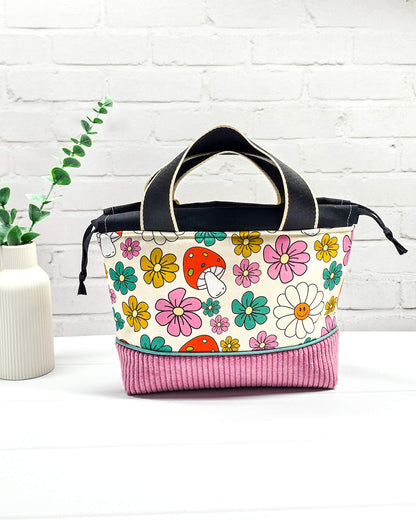 Handgemachte Projekttasche Alva in Größe S mit zwei Tragegriffen, bunten Retro-Pilzen und Blumen auf hellem Stoff und einem Taschenboden aus altrosa Breitcord. Handgenäht in Bayern von Nadelmikado. 