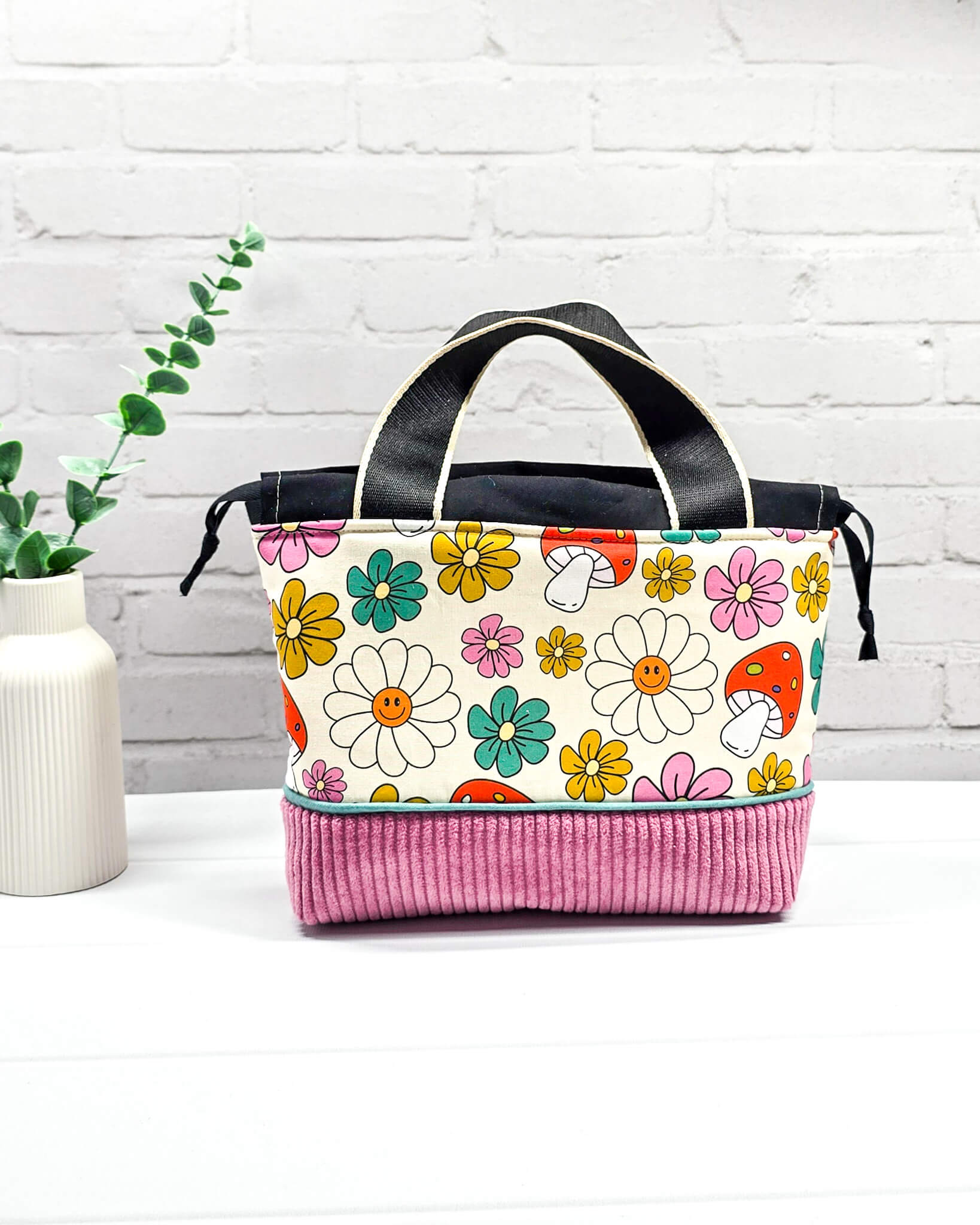 Handgemachte Projekttasche Alva in Größe S mit zwei Tragegriffen, bunten Retro-Pilzen und Blumen auf hellem Stoff und einem Taschenboden aus altrosa Breitcord. Handgenäht in Bayern von Nadelmikado. 