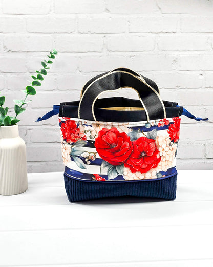 Projekttasche Alva in Größe S mit zwei Tragegriffen, roten Rosen auf blau-weiß gestreiftem Stoff und einem Taschenboden aus dunkelblauem Breitcord. Handgenäht in Bayern von Nadelmikado. 