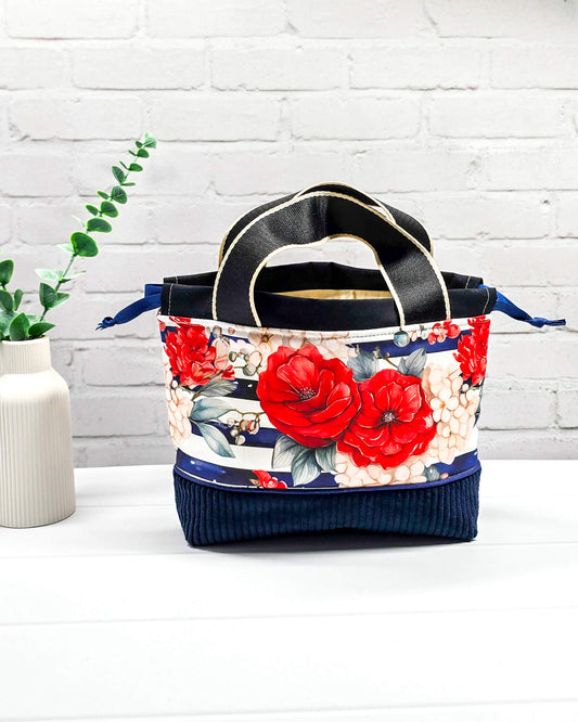 Projekttasche Alva in Größe S mit zwei Tragegriffen, roten Rosen auf blau-weiß gestreiftem Stoff und einem Taschenboden aus dunkelblauem Breitcord. Handgenäht in Bayern von Nadelmikado. 