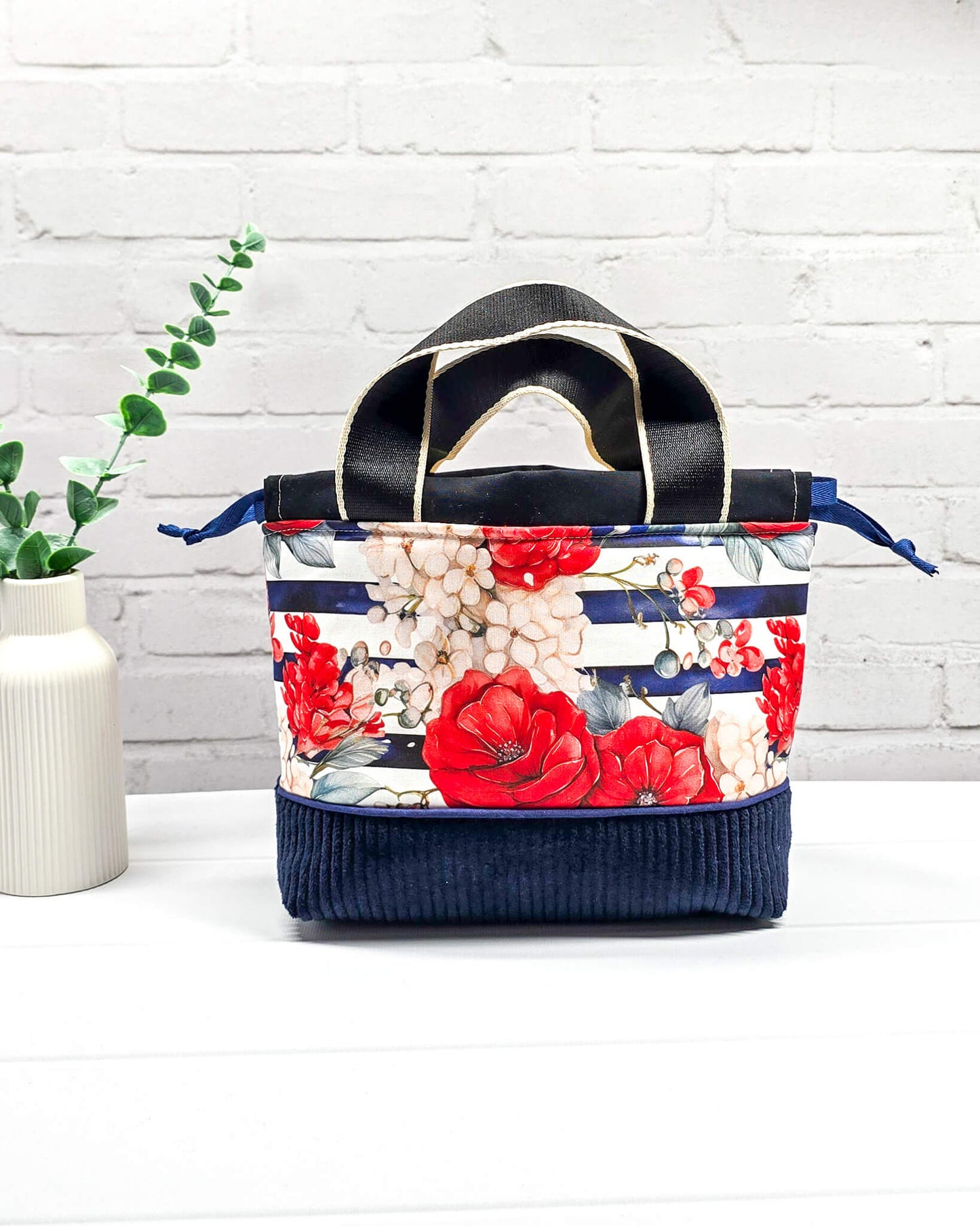 Projekttasche Alva in Größe S mit zwei Tragegriffen, roten Rosen auf blau-weiß gestreiftem Stoff und einem Taschenboden aus dunkelblauem Breitcord. Handgenäht in Bayern von Nadelmikado. 