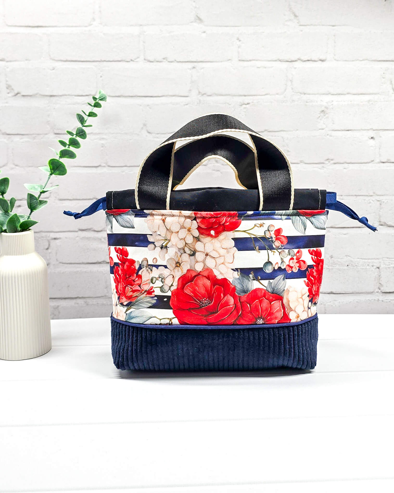 Projekttasche Alva in Größe S mit zwei Tragegriffen, roten Rosen auf blau-weiß gestreiftem Stoff und einem Taschenboden aus dunkelblauem Breitcord. Handgenäht in Bayern von Nadelmikado. 