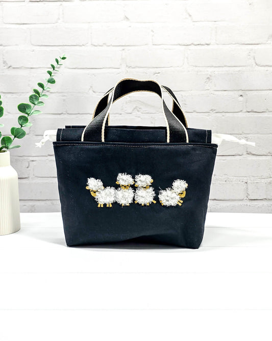 Projekttasche Alva S mit Schäfchenmotiv auf schwarzem Stoff, handgenäht in Bayern von Nadelmikado