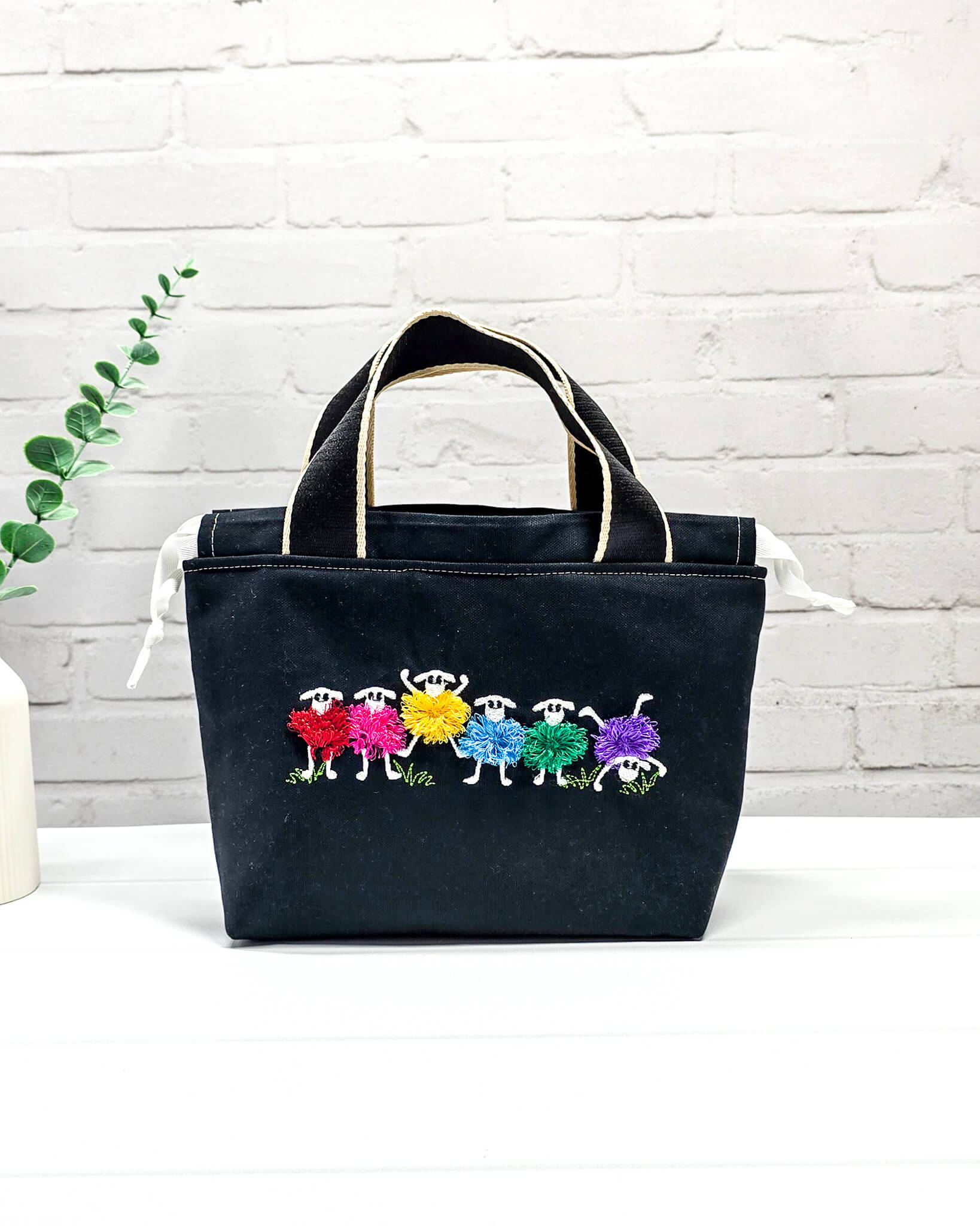 Projekttasche Alva S mit buntem Schafmotiv auf schwarzem Stoff, handgenäht in Bayern von Nadelmikado