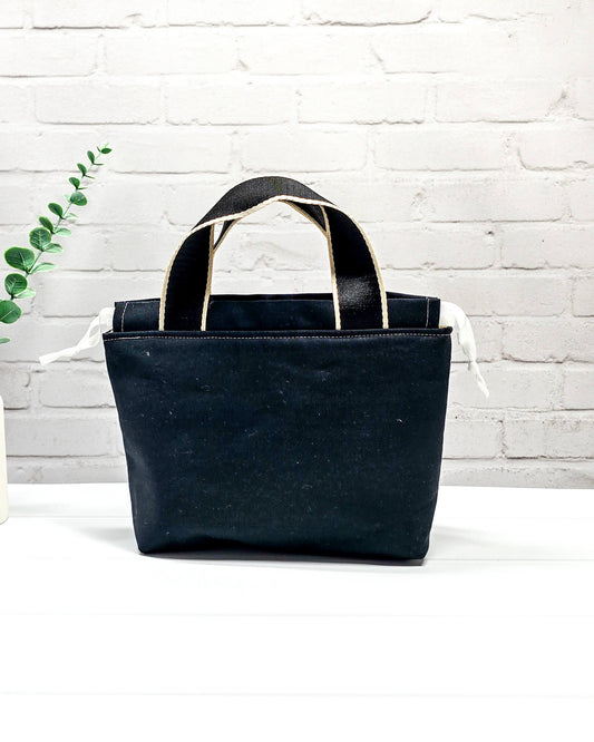 Projekttasche Alva S mit buntem Schafmotiv auf schwarzem Stoff, handgenäht in Bayern von Nadelmikado