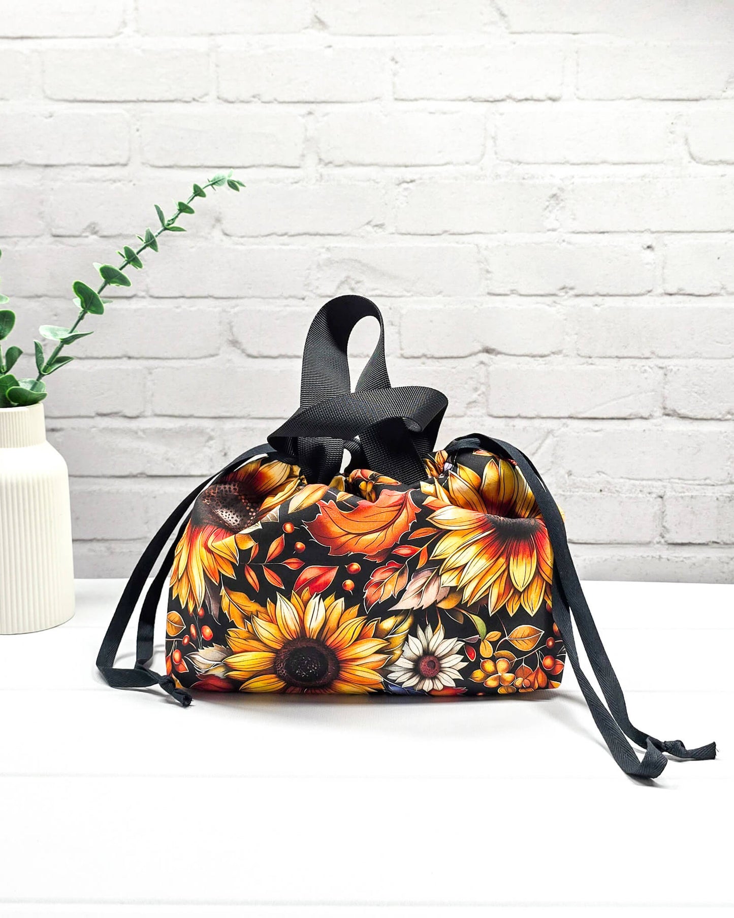 Projekttasche Alva S mit großen gelben Sonnenblumen und orangefarbenen Herbstblättern auf dunklem Grund. Handgenäht in Bayern von Nadelmikado