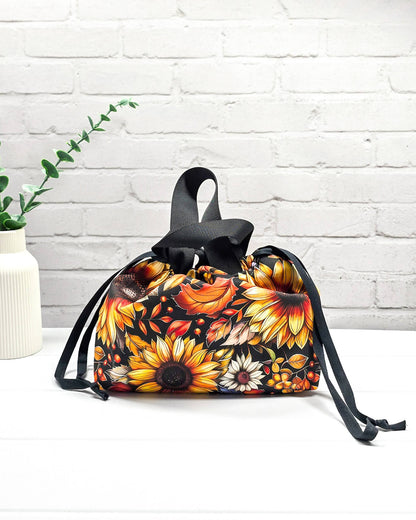 Projekttasche Alva S mit großen gelben Sonnenblumen und orangefarbenen Herbstblättern auf dunklem Grund. Handgenäht in Bayern von Nadelmikado