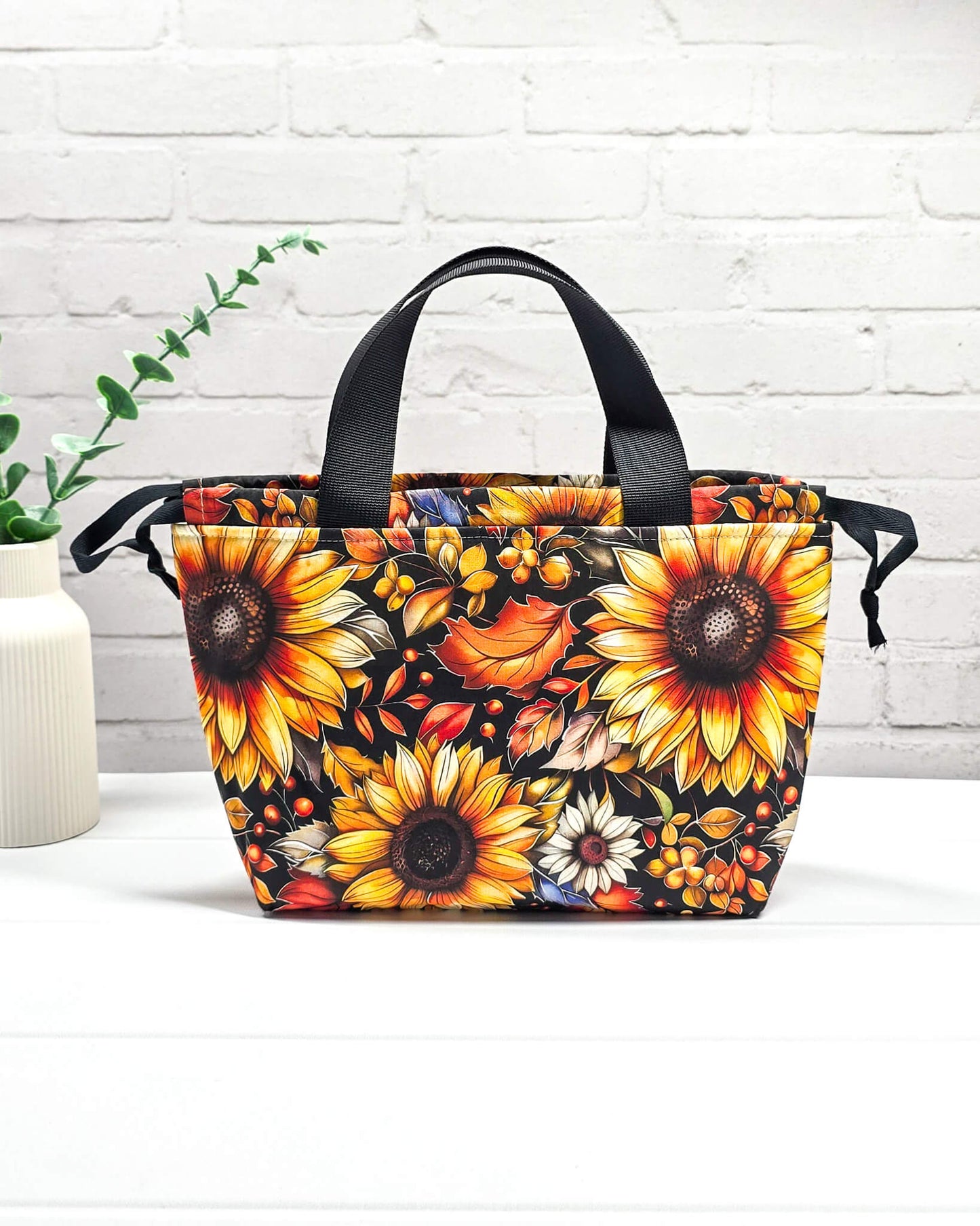 Projekttasche Alva S mit großen gelben Sonnenblumen und orangefarbenen Herbstblättern auf dunklem Grund. Handgenäht in Bayern von Nadelmikado
