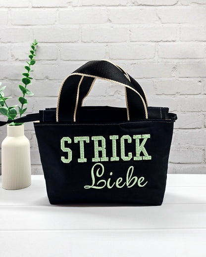 Projekttasche Alva S aus schwarzem Canvas mit mintgrüner 3D-Stickerei Strickliebe, Henkeln und schwarzem Kordelzugkragen. Handgenäht in Bayern von Nadelmikado.