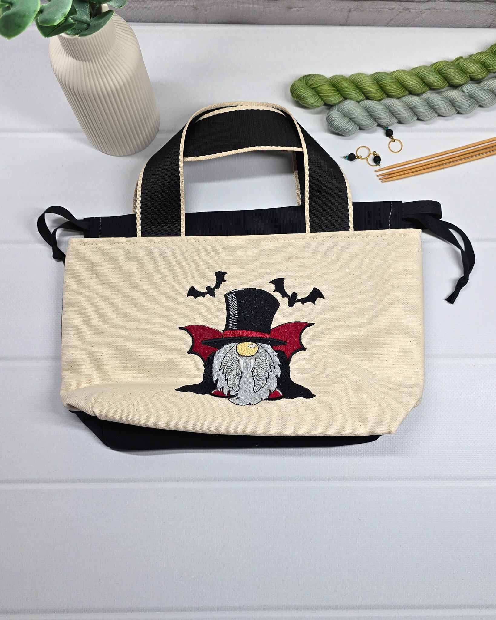 Projekttasche Alva S aus hellem Canvas mit gesticktem Vampir-Wichtel und Fledermäusen, Henkeln und schwarzem Kordelzug. Handgenäht in Bayern von Nadelmikado.