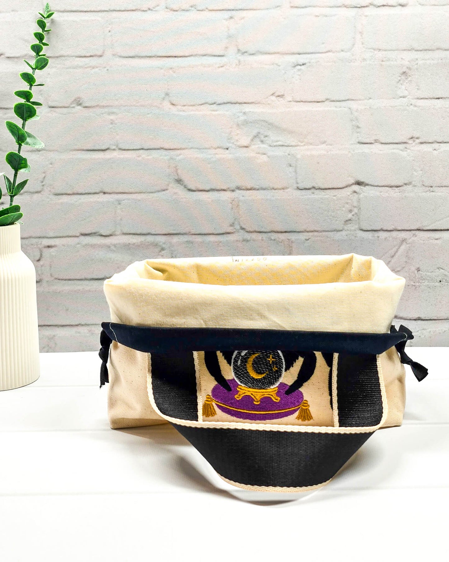 Projekttasche Alva S aus hellem Canvas mit gestickter Wahrsager Spinne und Kristallkugel, Henkeln und schwarzem Kordelzugkragen. Handgenäht in Bayern von Nadelmikado.