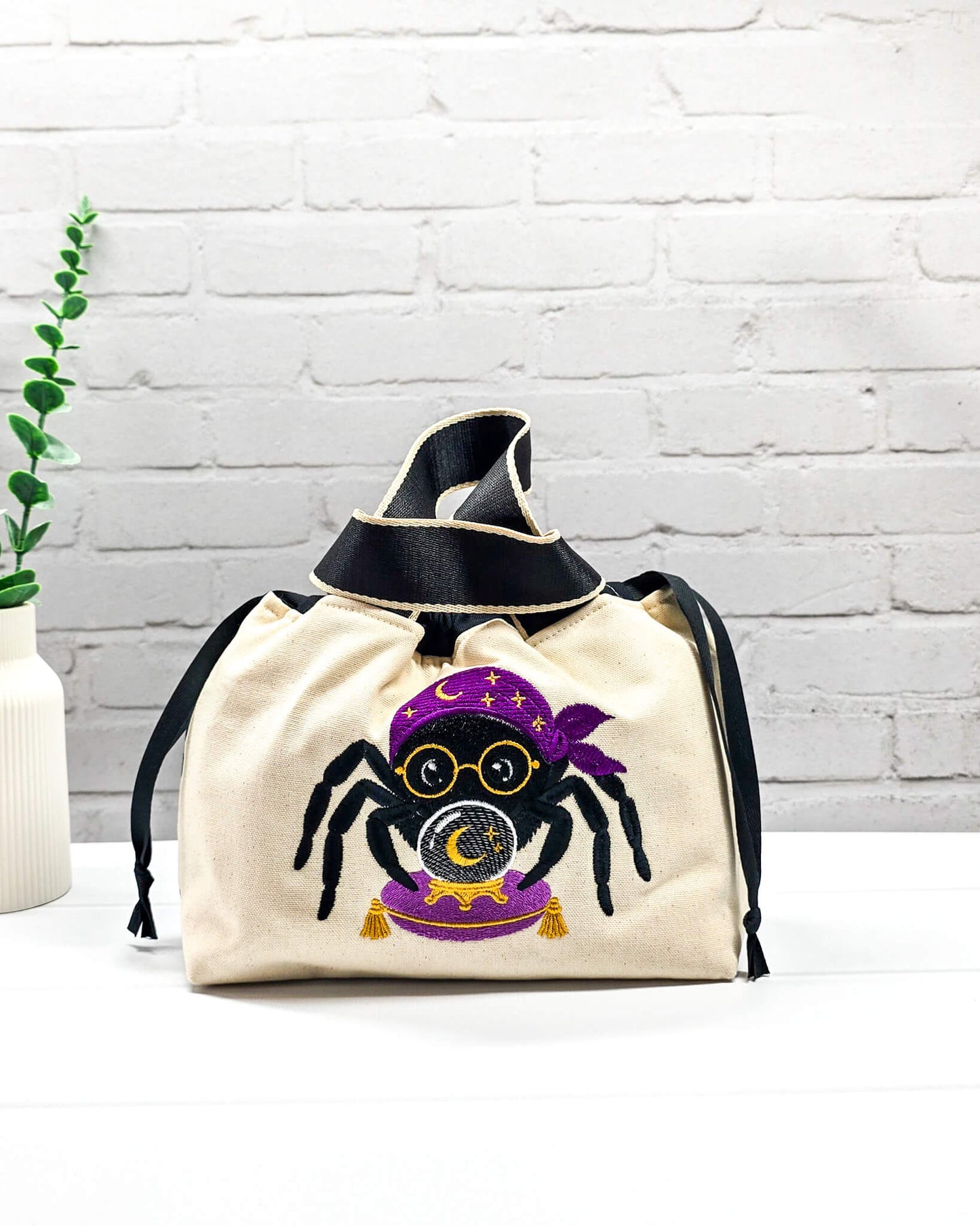 Projekttasche Alva S aus hellem Canvas mit gestickter Wahrsager Spinne und Kristallkugel, Henkeln und schwarzem Kordelzugkragen. Handgenäht in Bayern von Nadelmikado.