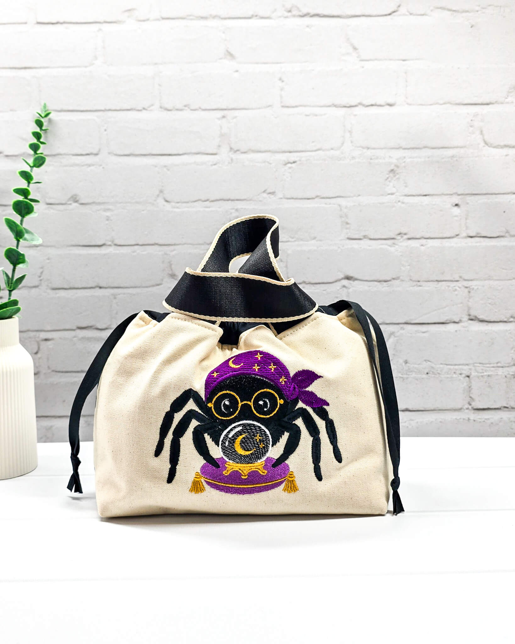 Projekttasche Alva S aus hellem Canvas mit gestickter Wahrsager Spinne und Kristallkugel, Henkeln und schwarzem Kordelzugkragen. Handgenäht in Bayern von Nadelmikado.