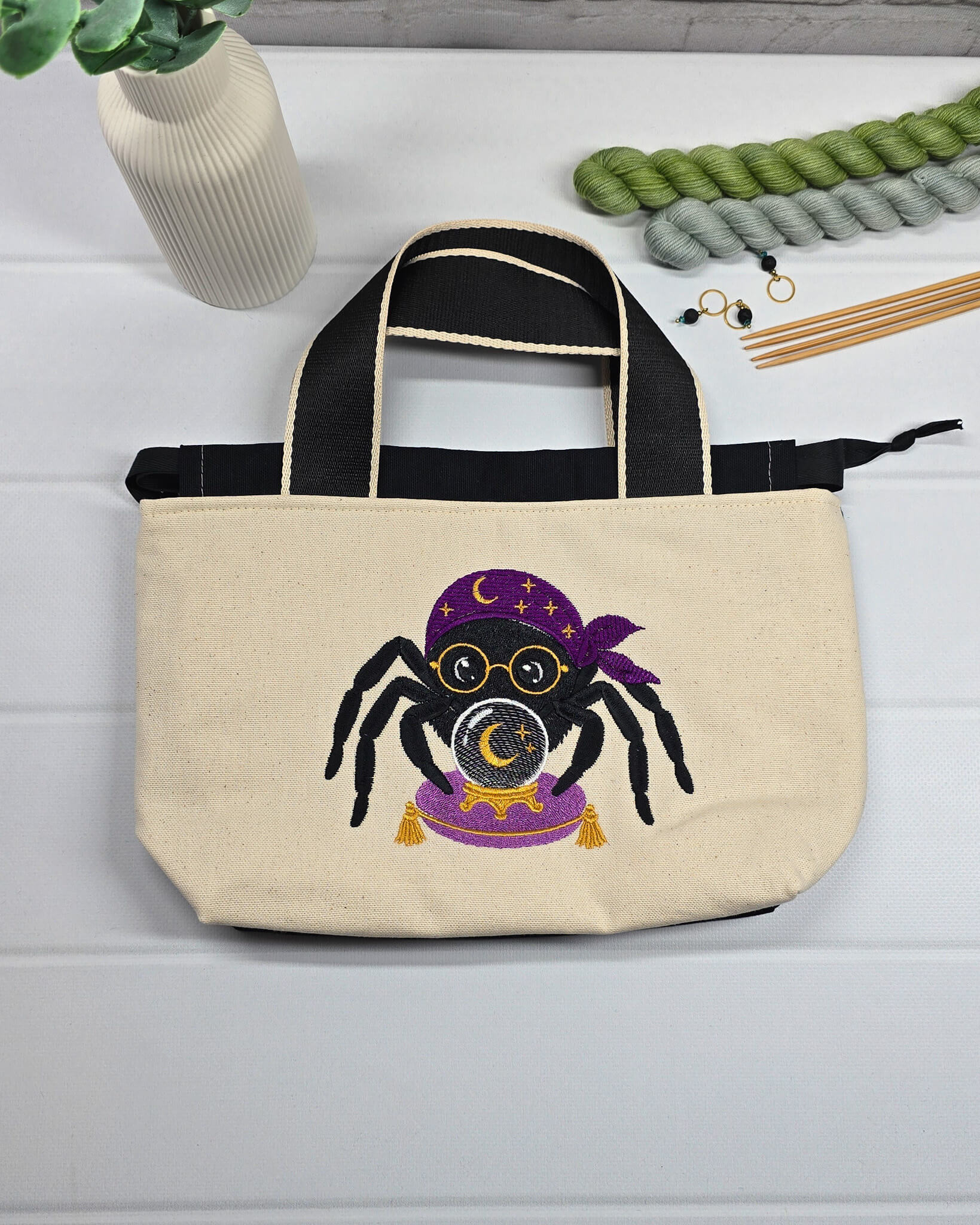 Projekttasche Alva S aus hellem Canvas mit gestickter Wahrsager Spinne und Kristallkugel, Henkeln und schwarzem Kordelzugkragen. Handgenäht in Bayern von Nadelmikado.