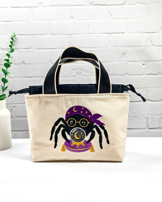 Projekttasche Alva S aus hellem Canvas mit gestickter Wahrsager Spinne und Kristallkugel, Henkeln und schwarzem Kordelzugkragen. Handgenäht in Bayern von Nadelmikado.