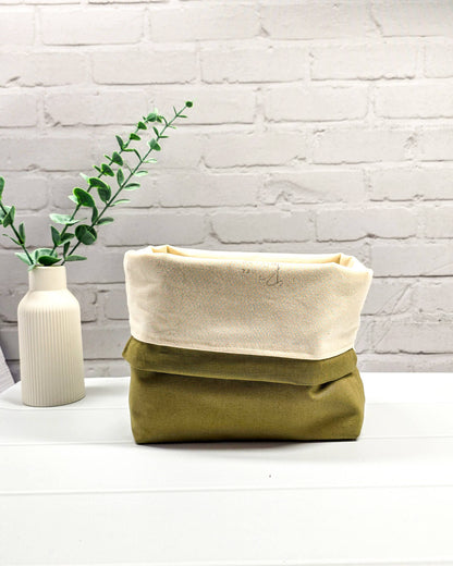 Projekttasche mit Kordelzug und cremefarbenem Tragegurt aus dunkelgrünem Stoff mit kleinen Blüten und Trankflaschen sowie olivgrünem Boden. Bietet Platz für 400g Wolle und schützt das Strickzeug vor Verheddern. Handgenäht in Bayern von Nadelmikado.