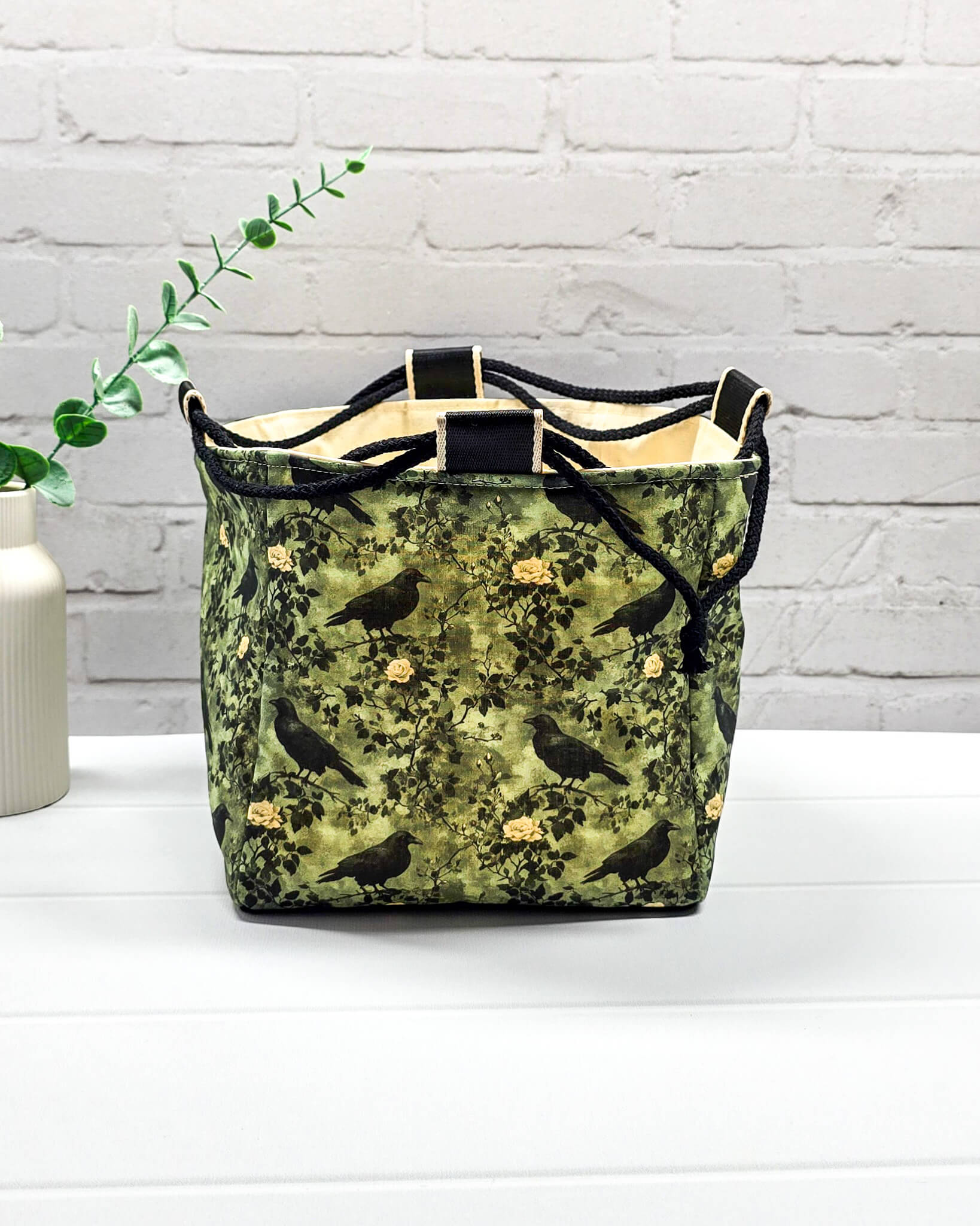 Mittlere grüne Projekttasche mit Kordelzug im Rice Bag Stil, gemustert mit Raben und Rosen, genutzt als Strickbeutel für ein Tuchprojekt mit bis zu 400g Wolle. Handgenäht in Bayern  von Nadelmikado.
