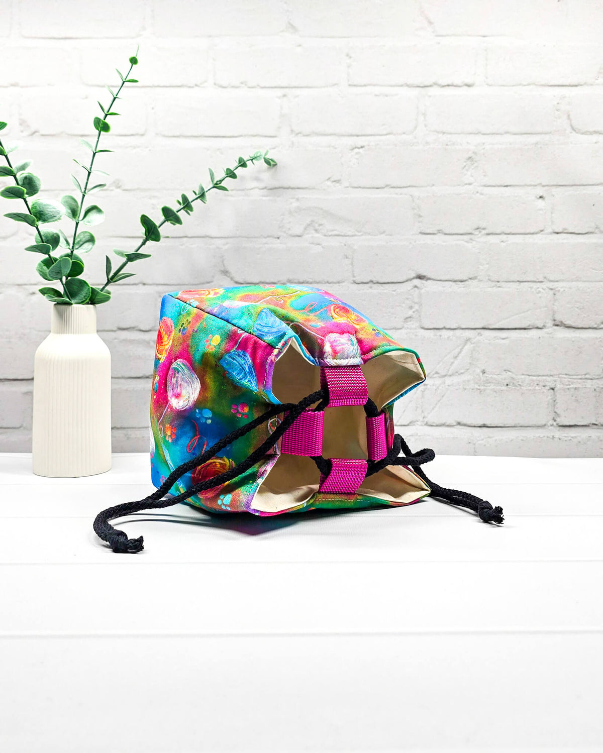 Projekttasche Aska Größe S als Rice Bag mit bunten Wollknäueln auf leuchtendem Stoff in Pink, Türkis, Blau und Grün. Mit schwarzem Kordelzug und pinker Schlaufe. Handgenäht in Bayern von Nadelmikado.