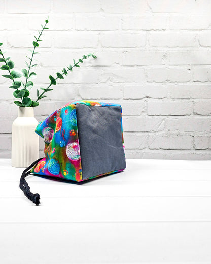 Projekttasche Aska Größe S als Rice Bag mit bunten Wollknäueln auf leuchtendem Stoff in Pink, Türkis, Blau und Grün. Mit schwarzem Kordelzug und pinker Schlaufe. Handgenäht in Bayern von Nadelmikado.