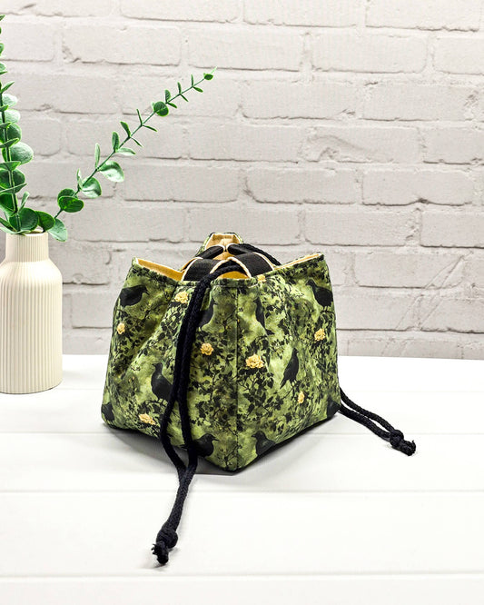 Kleine grüne Projekttasche mit Kordelzug im Rice Bag Stil, gemustert mit Raben und Rosen, genutzt als Strickbeutel für ein Sockenstrickprojekt mit Wolle und Nadelspiel. Handgenäht in Bayern von Nadelmikado.