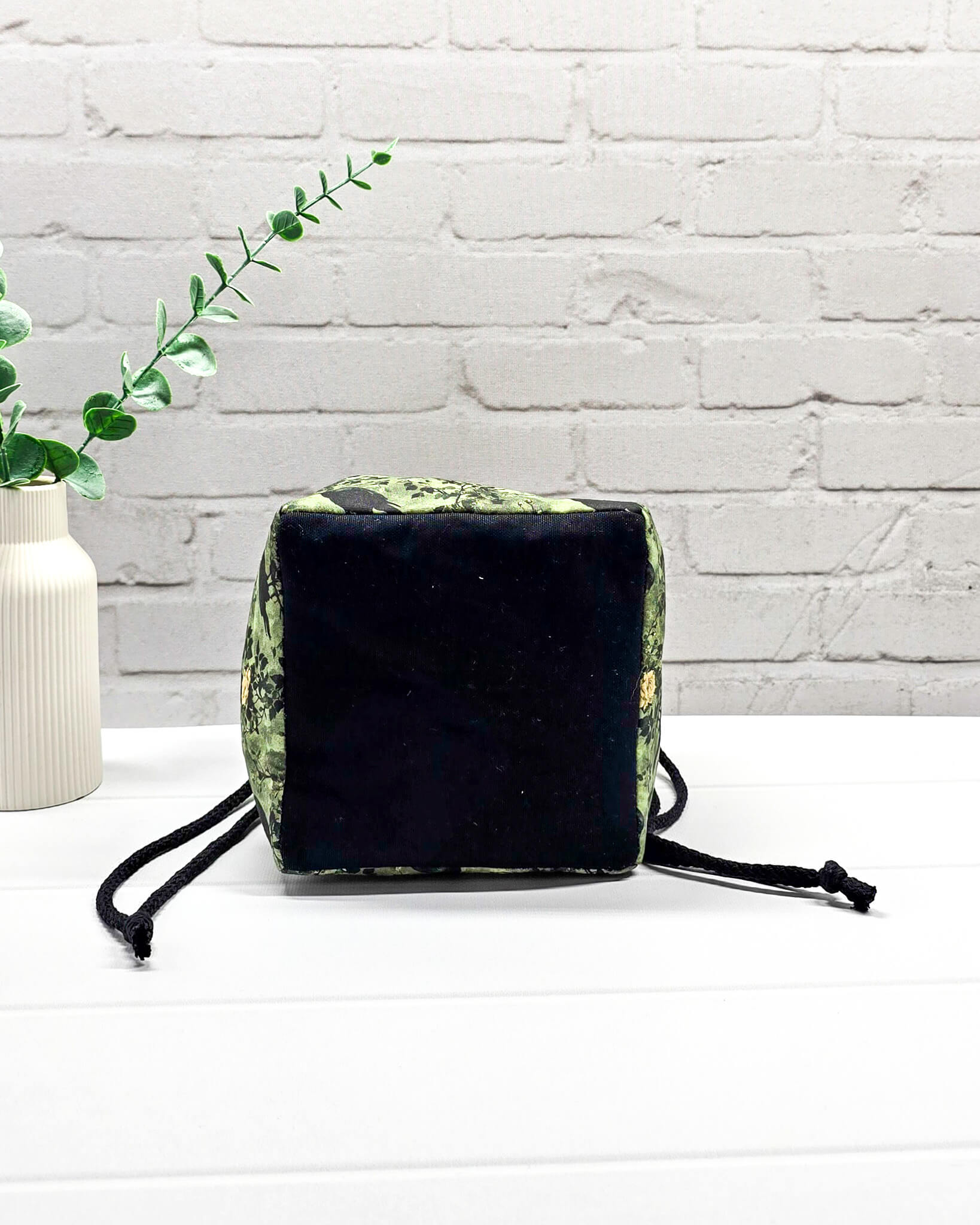 Kleine grüne Projekttasche mit Kordelzug im Rice Bag Stil, gemustert mit Raben und Rosen, genutzt als Strickbeutel für ein Sockenstrickprojekt mit Wolle und Nadelspiel. Handgenäht in Bayern von Nadelmikado.