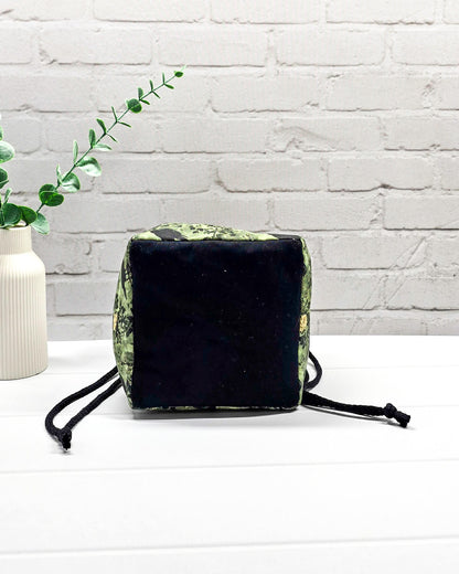 Kleine grüne Projekttasche mit Kordelzug im Rice Bag Stil, gemustert mit Raben und Rosen, genutzt als Strickbeutel für ein Sockenstrickprojekt mit Wolle und Nadelspiel. Handgenäht in Bayern von Nadelmikado.