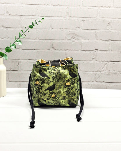 Kleine grüne Projekttasche mit Kordelzug im Rice Bag Stil, gemustert mit Raben und Rosen, genutzt als Strickbeutel für ein Sockenstrickprojekt mit Wolle und Nadelspiel. Handgenäht in Bayern von Nadelmikado.