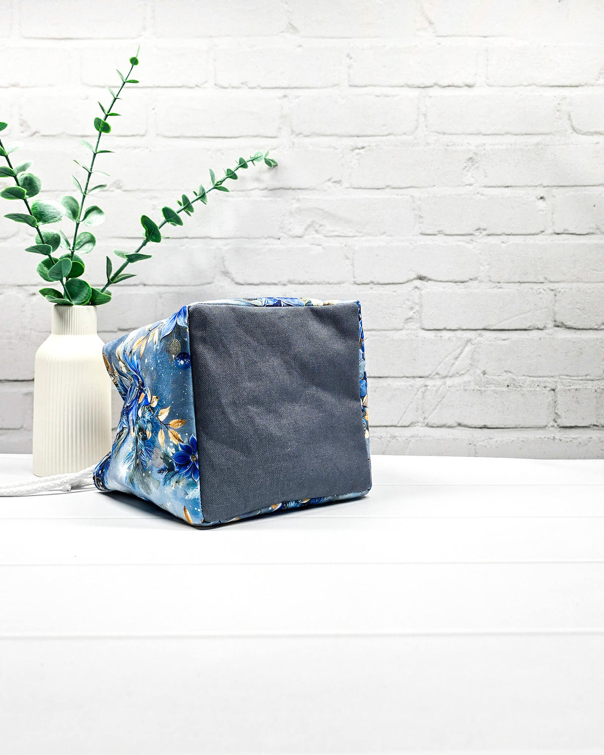 Projekttasche Aska Größe S als Rice Bag mit blauem Winterblütenmotiv und goldenen Akzenten auf hellem Hintergrund. Mit weißem Kordelzug und blauen Schlaufen. Handgenäht in Bayern von Nadelmikado.