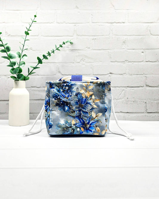 Projekttasche Aska Größe S als Rice Bag mit blauem Winterblütenmotiv und goldenen Akzenten auf hellem Hintergrund. Mit weißem Kordelzug und blauen Schlaufen. Handgenäht in Bayern von Nadelmikado.