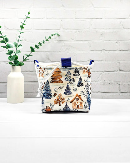 Projekttasche Aska Größe S als Rice Bag aus weißem Stoff mit blauen Tannenbäumen, Lebkuchenhäuschen und winterlichen Zweigen. Mit weißem Kordelzug und blauen Schlaufen. Handgenäht in Bayern von Nadelmikado.