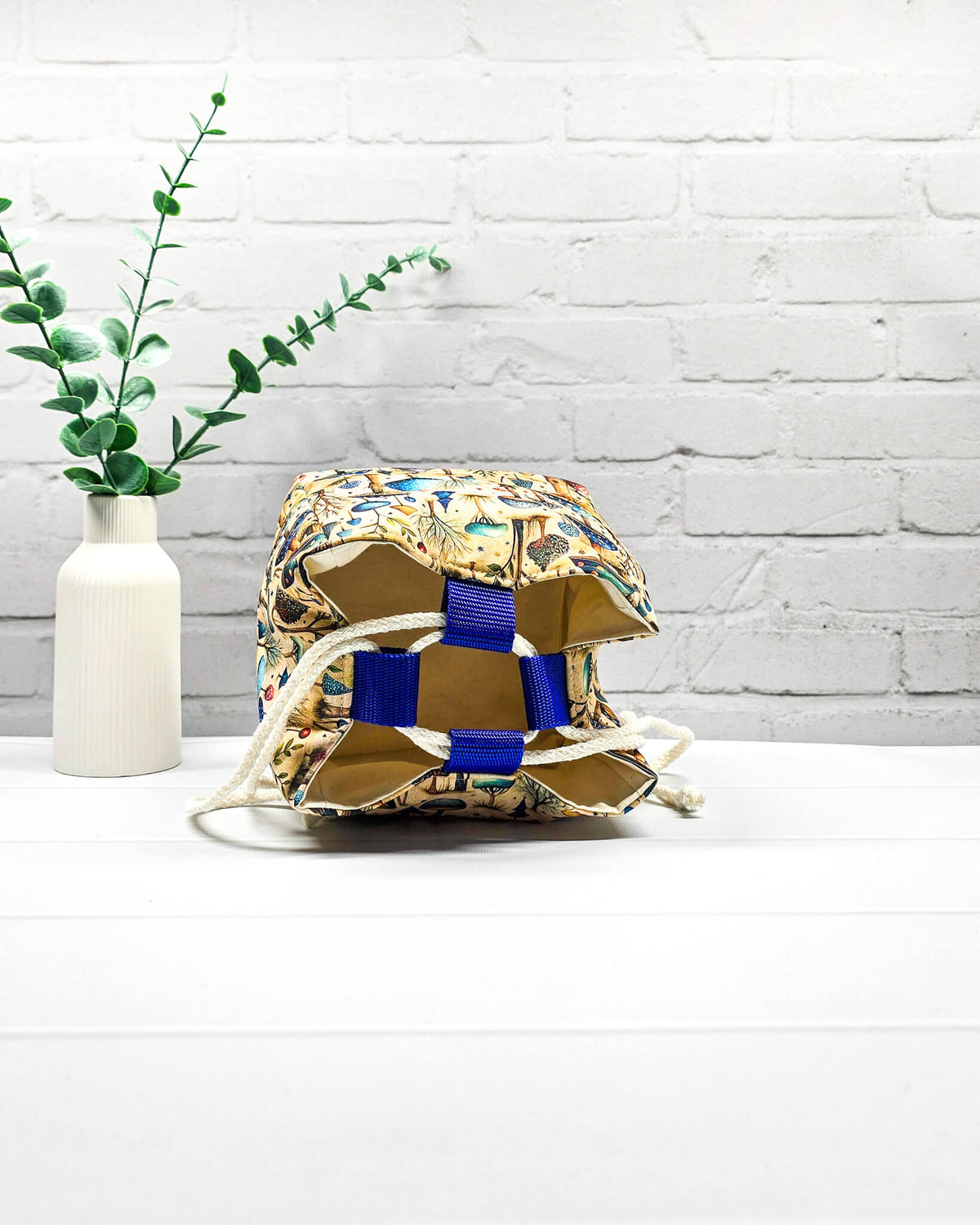Projekttasche Aska Größe S als Rice Bag mit bunten Pilzen, kleinen Bäumen und Waldpflanzen in Blau, Türkis und Grün auf beigefarbenem Stoff. Mit heller Kordel und blauen Schlaufen. Handgenäht in Bayern von Nadelmikado.