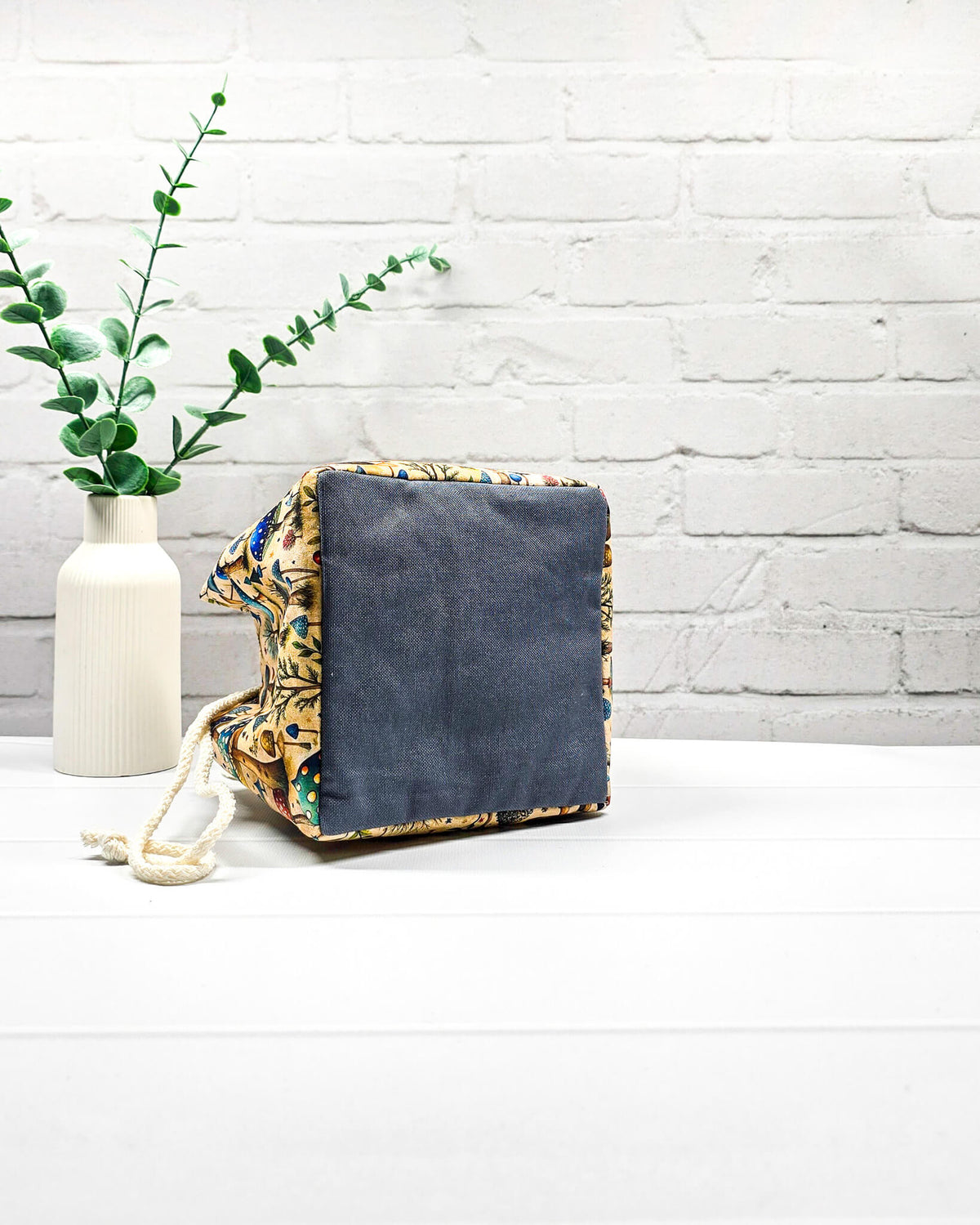 Projekttasche Aska Größe S als Rice Bag mit bunten Pilzen, kleinen Bäumen und Waldpflanzen in Blau, Türkis und Grün auf beigefarbenem Stoff. Mit heller Kordel und blauen Schlaufen. Handgenäht in Bayern von Nadelmikado.