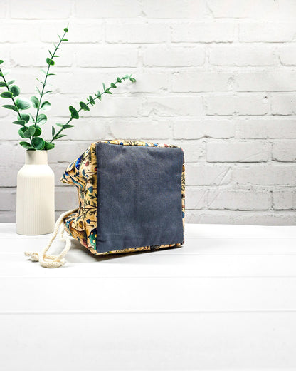 Projekttasche Aska Größe S als Rice Bag mit bunten Pilzen, kleinen Bäumen und Waldpflanzen in Blau, Türkis und Grün auf beigefarbenem Stoff. Mit heller Kordel und blauen Schlaufen. Handgenäht in Bayern von Nadelmikado.