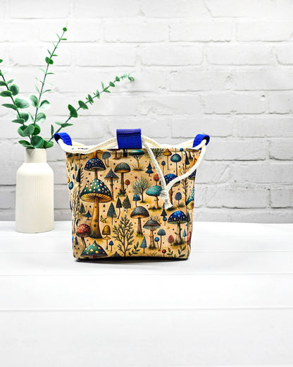 Projekttasche Aska Größe S als Rice Bag mit bunten Pilzen, kleinen Bäumen und Waldpflanzen in Blau, Türkis und Grün auf beigefarbenem Stoff. Mit heller Kordel und blauen Schlaufen. Handgenäht in Bayern von Nadelmikado.