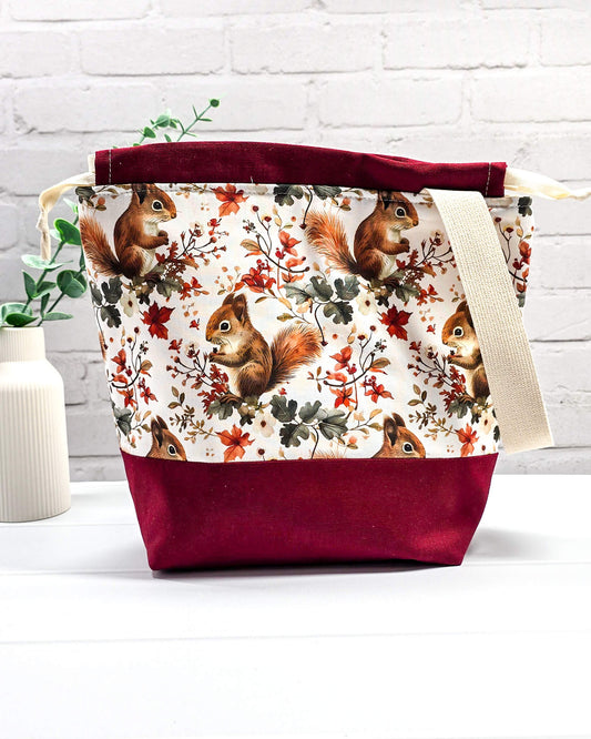 Handgenähte Projekttasche mit herbstlichem Eichhörnchen-Muster auf hellem Grund mit weinrotem Boden. Handmade in Bayern von Nadelmikado.