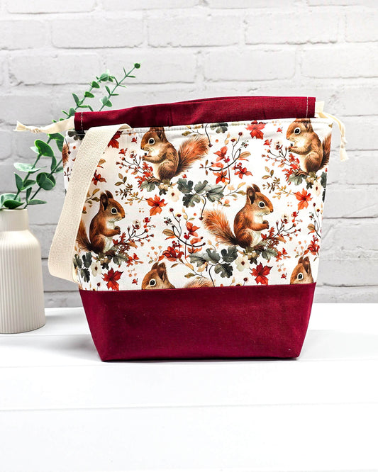 Handgenähte Projekttasche mit herbstlichem Eichhörnchen-Muster auf hellem Grund mit weinrotem Boden. Handmade in Bayern von Nadelmikado.