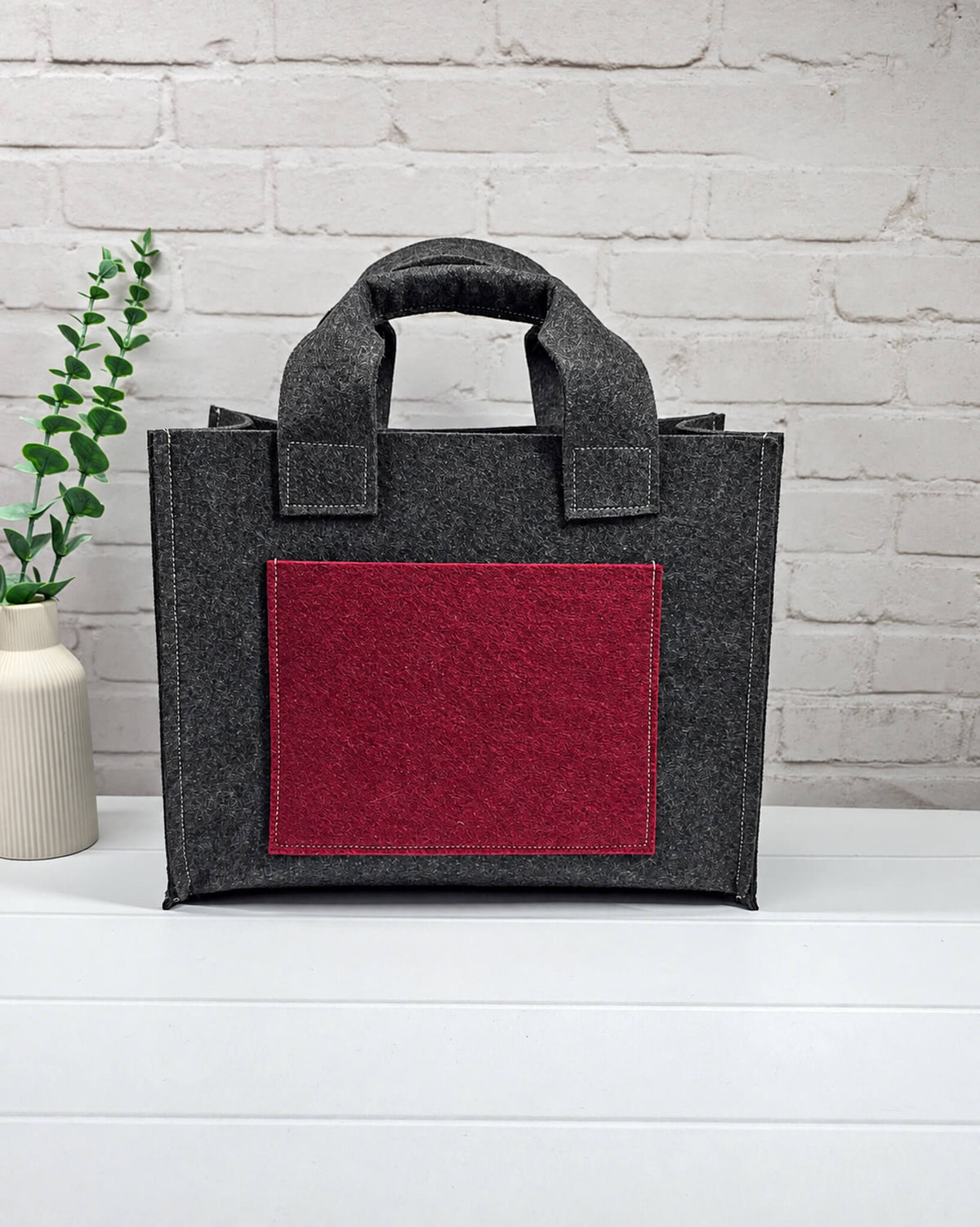 Stricktasche Größe M aus anthrazitfarbenem Filz mit großer bordeauxroter Außentasche und zwei kurzen Henkeln. Handgenäht in Bayern von Nadelmikado.