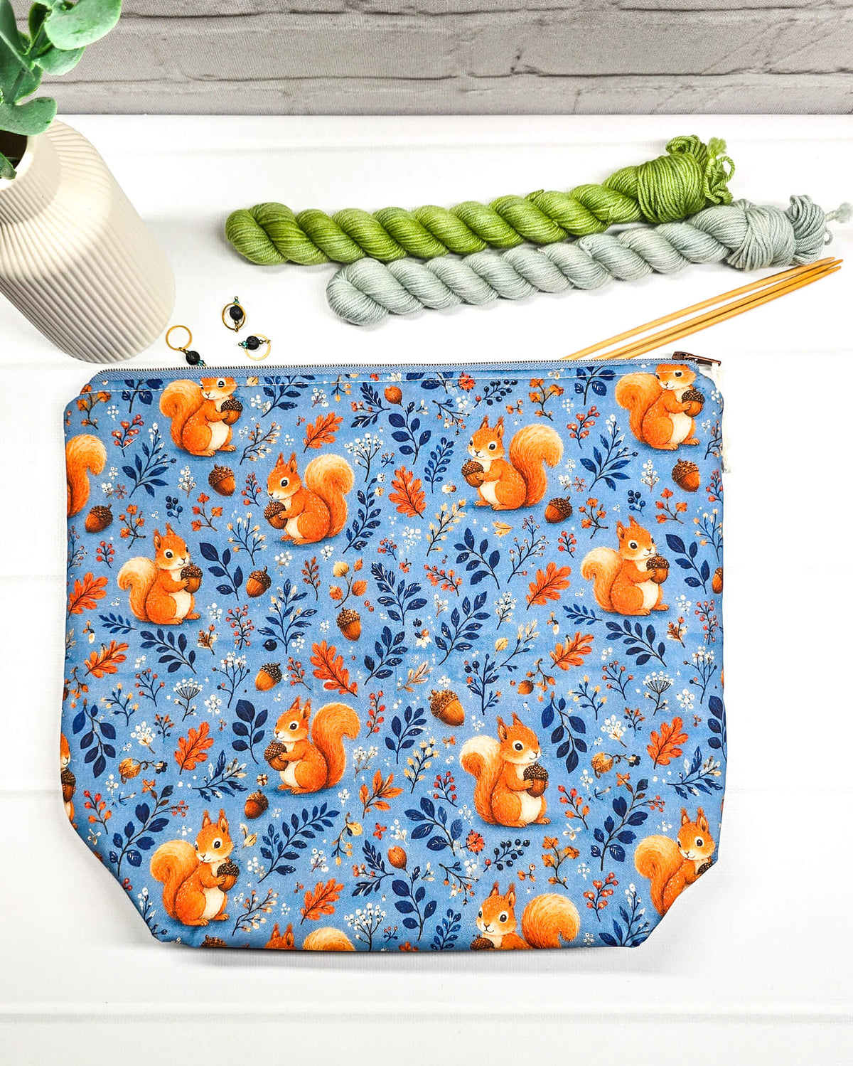 Projekttasche Größe M mit Reißverschluss aus blauem Baumwollstoff mit orangefarbenen Eichhörnchen, Eicheln und Blättern zur Aufbewahrung von Wolle und Strickprojekten. Handgenäht in Bayern von Nadelmikado.