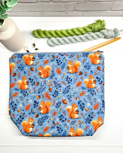 Projekttasche Größe M mit Reißverschluss aus blauem Baumwollstoff mit orangefarbenen Eichhörnchen, Eicheln und Blättern zur Aufbewahrung von Wolle und Strickprojekten. Handgenäht in Bayern von Nadelmikado.
