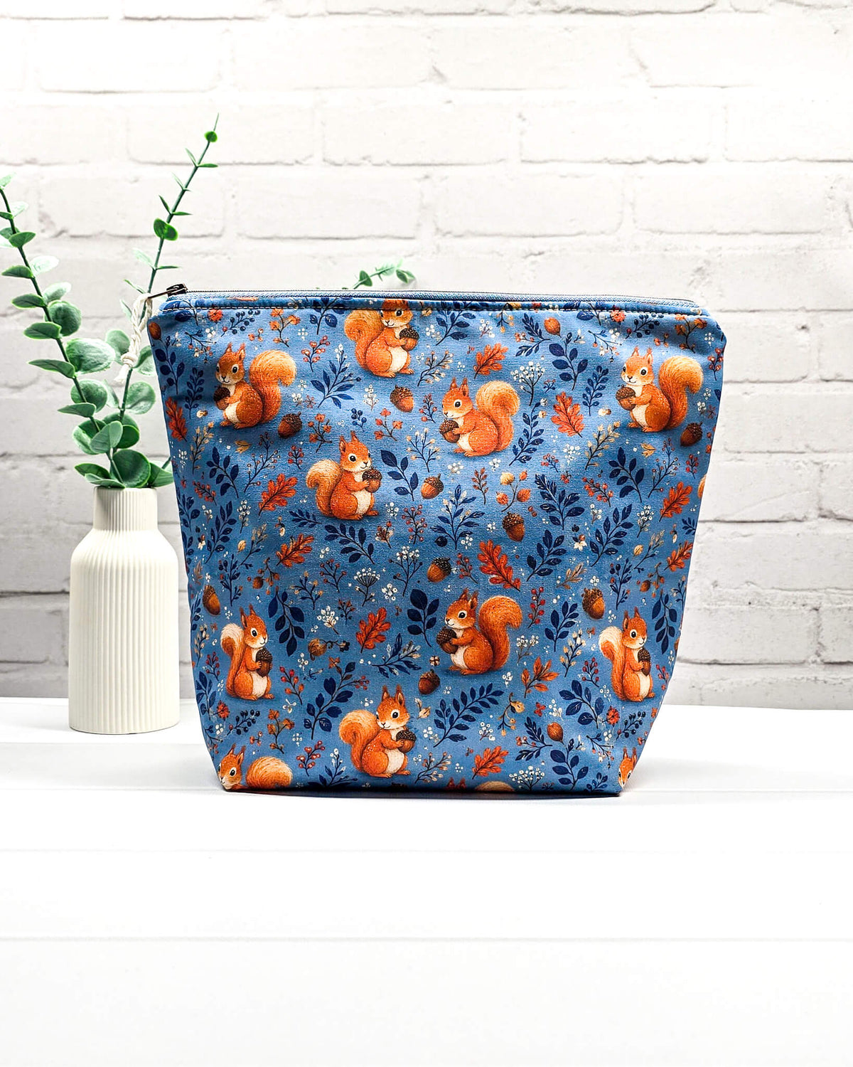 Projekttasche Größe M mit Reißverschluss aus blauem Baumwollstoff mit orangefarbenen Eichhörnchen, Eicheln und Blättern zur Aufbewahrung von Wolle und Strickprojekten. Handgenäht in Bayern von Nadelmikado.